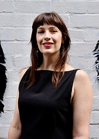 photograph of a woman from the waist up against a plain brick wall.