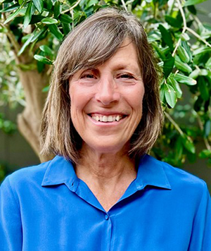 head shot of a woman standing in frontof a bush