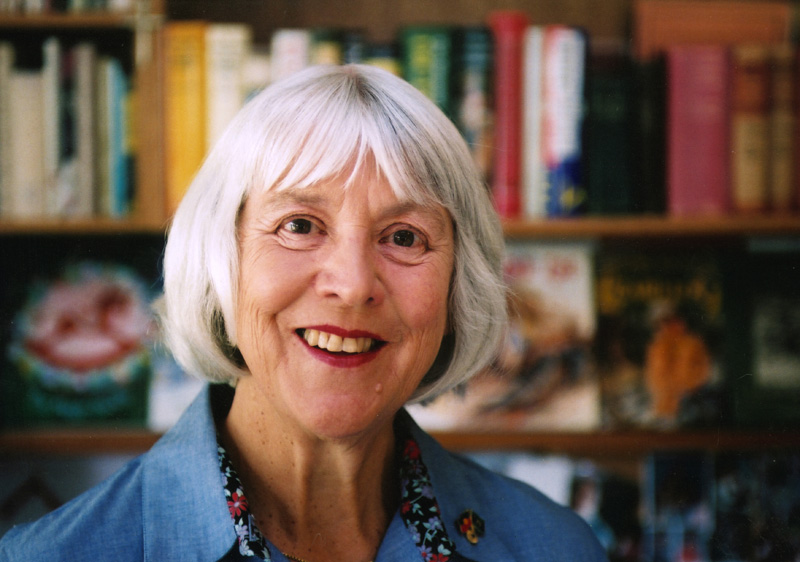 Photo of Christobel Mattingley, white haired lady standing in front of a bookshelf